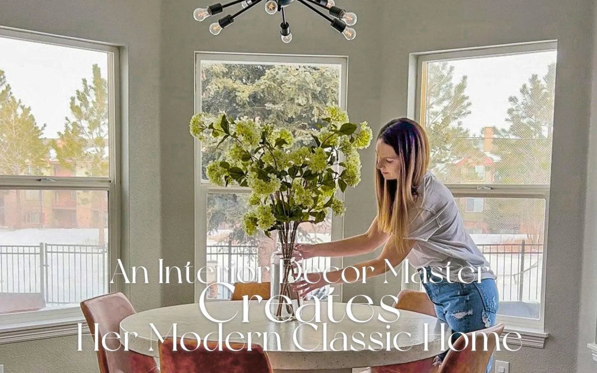 Woman arranging green floral centerpiece on round dining table in bright, modern living room with large windows