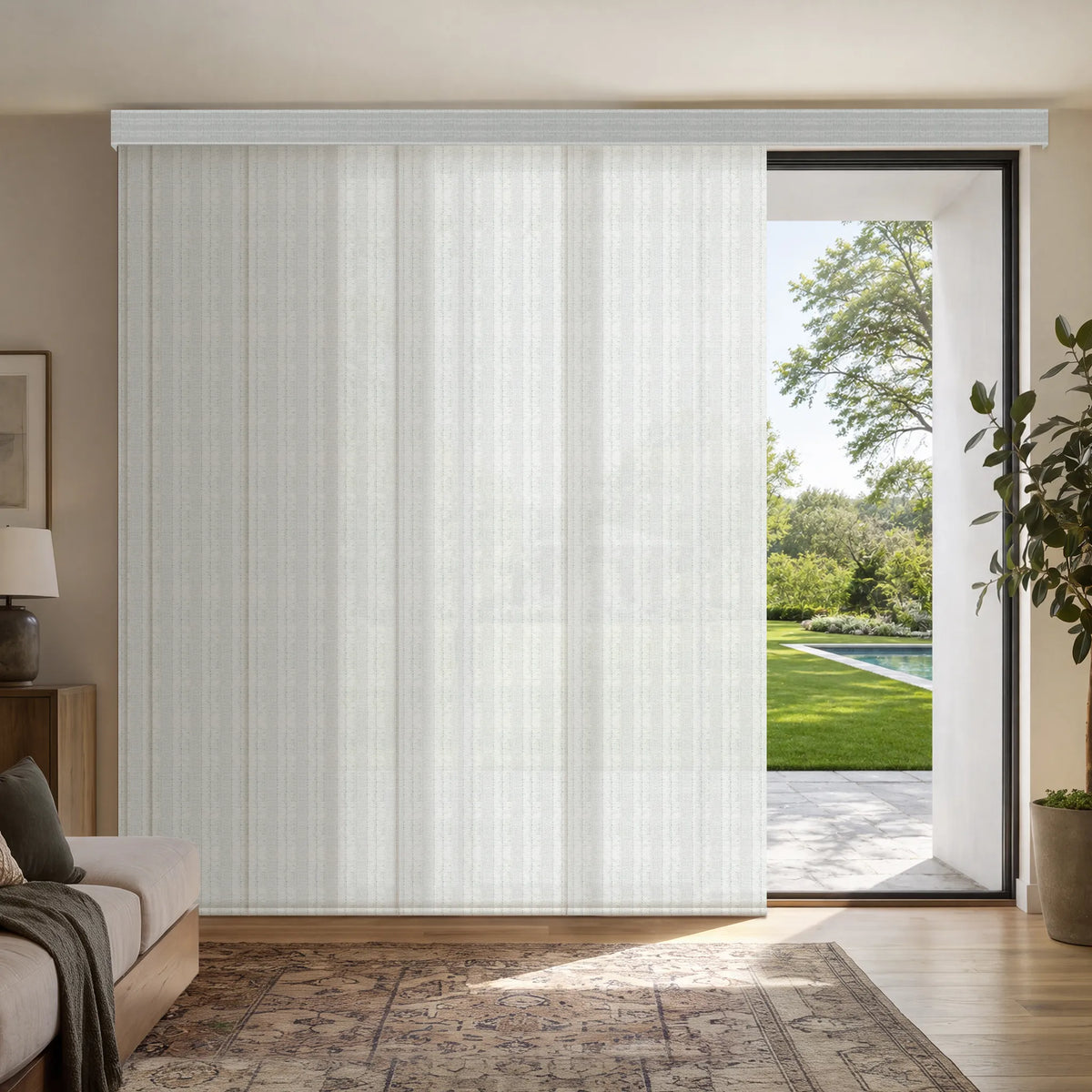 A large white Motorized Light Filtering Panel Track Blinds Installed in a modern living room, with a glass door open to a green backyard and pool area.