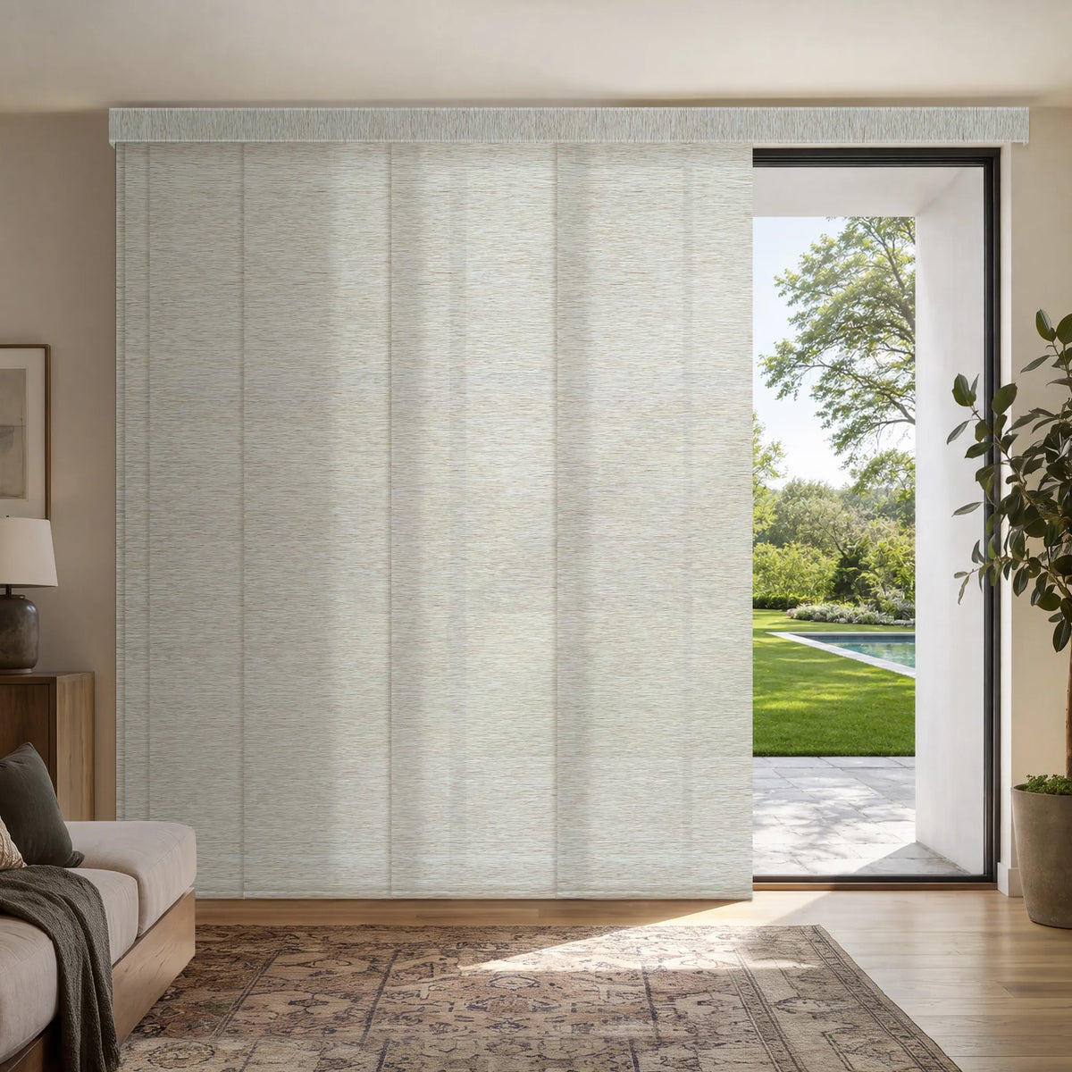 A light beige Motorized Light Filtering Panel Track Blinds window shade partially drawn over a large glass sliding door in a modern living room setting with a pool visible outside.