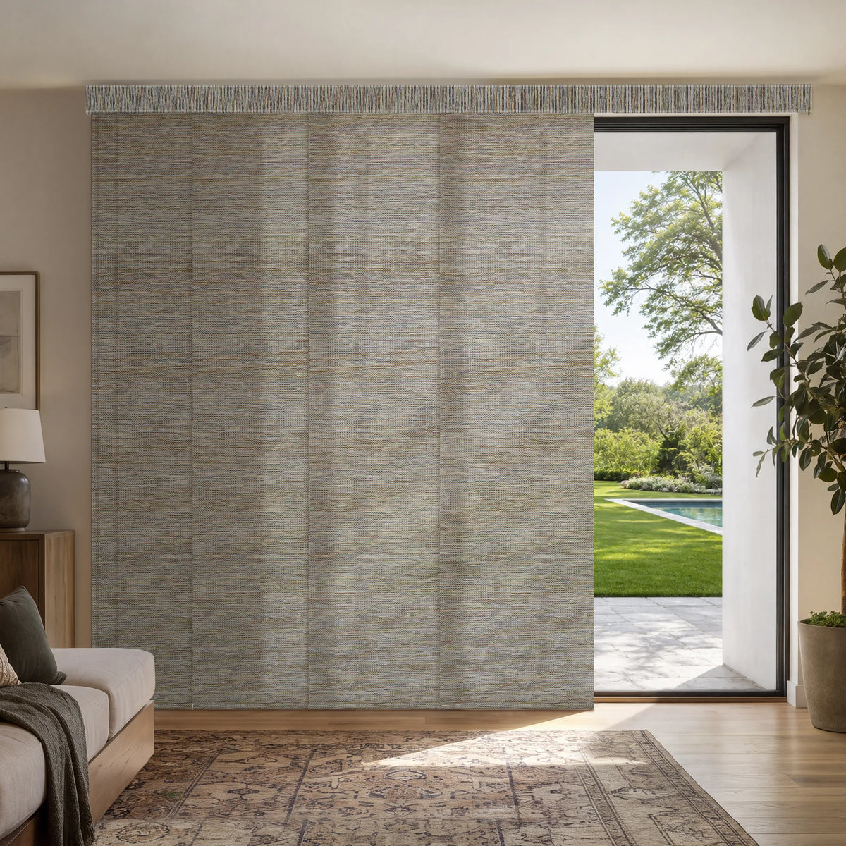 A large Motorized Light Filtering Panel Track Blinds with a textured, heathered gray and beige fabric, shown installed in a modern living room setting with a sliding glass door leading to a green backyard.