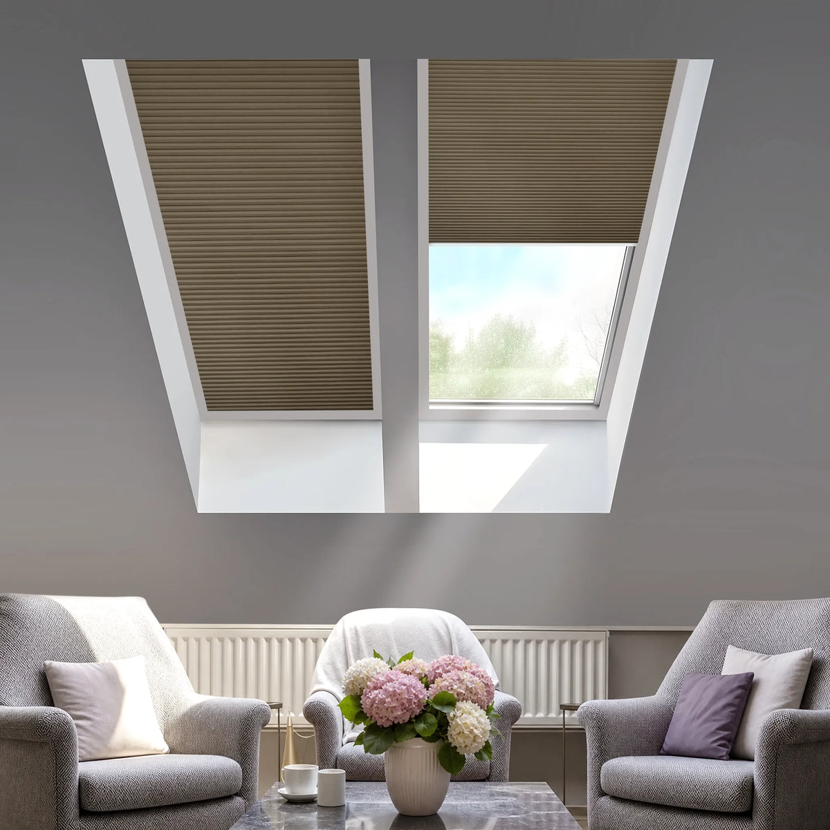 Two coffee cellular roller blind window treatments installed on a sloped attic ceiling, shown in a modern living room setting with gray armchairs and a coffee table below.