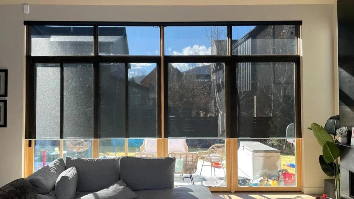 Modern living room with large windows, smart roller shades, and sunlight filtering in.