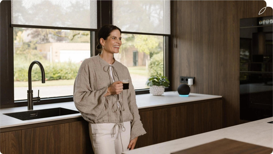 The high-end kitchen is equipped with motionblinds roller shades. The woman drinks coffee in front of the window.