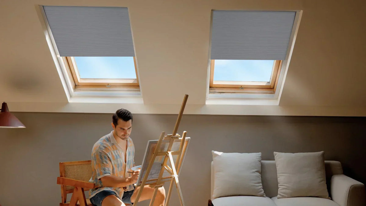 The attic scene, equipped with skylight shades, shows a man engaged in painting, with an intense artistic atmosphere.