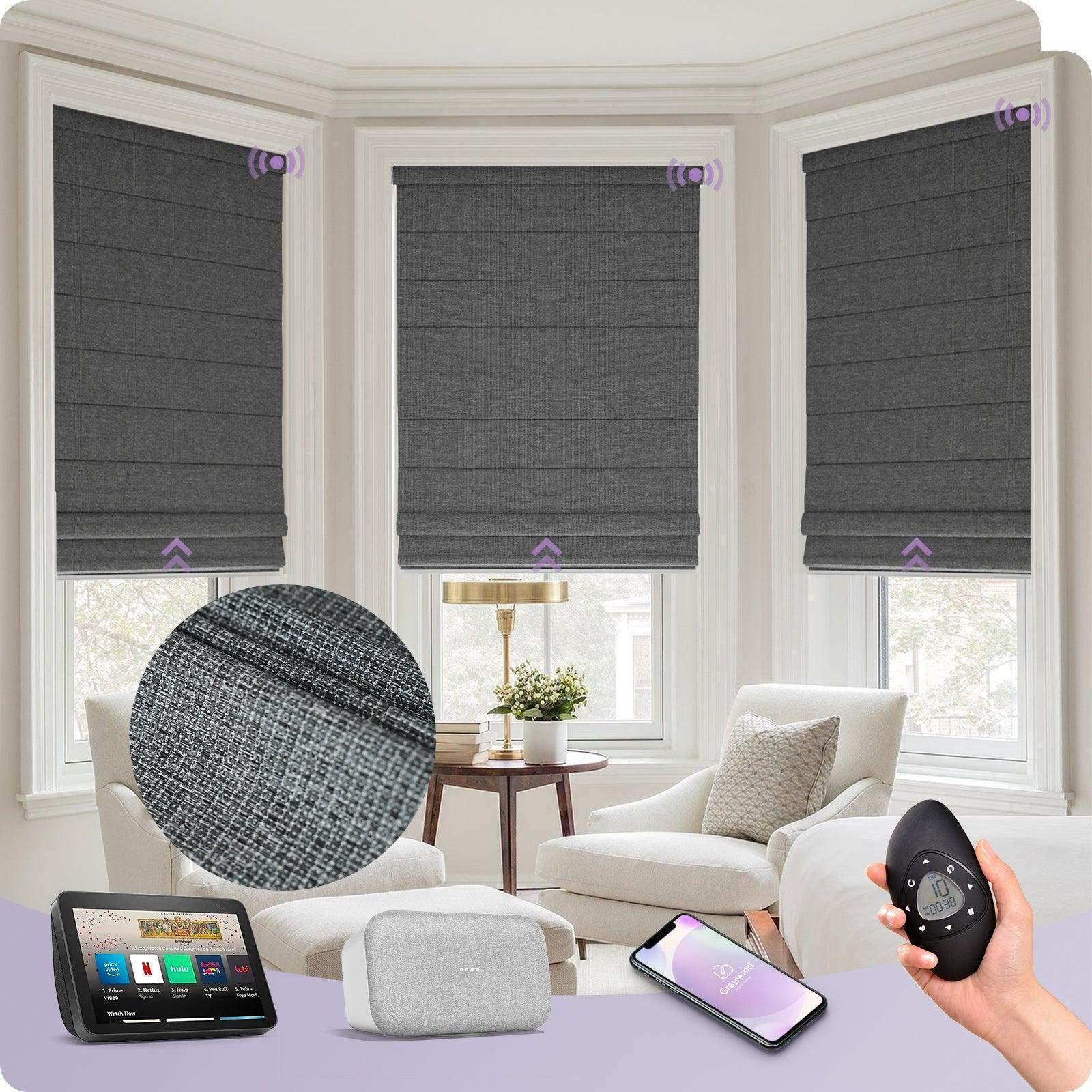 Smart gray fabric motorized Roman shades on bay windows in a bright living room, controlled by remote, smartphone, and smart home devices.