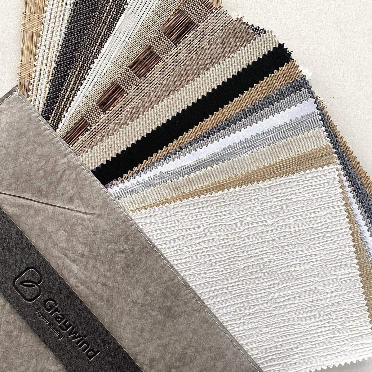 Assorted window treatment fabric swatches in neutral colors and textures displayed in a sample book.