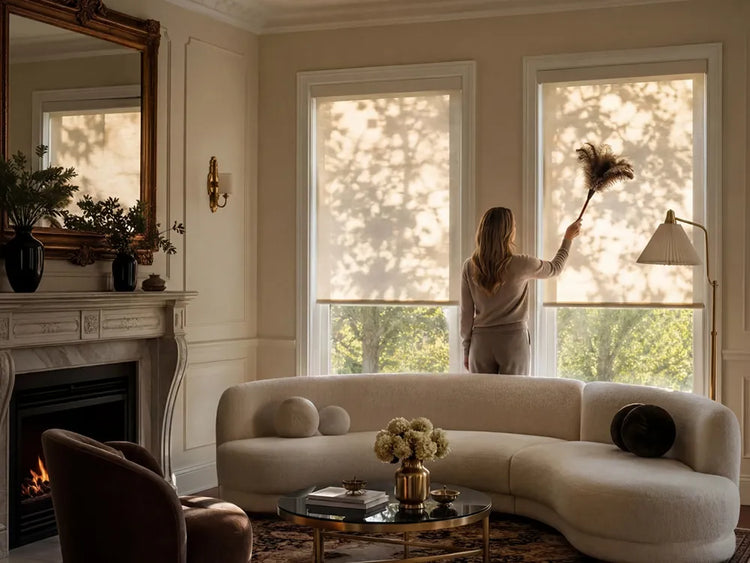 a woman is cleaning a roller shades by a Feather duster 
