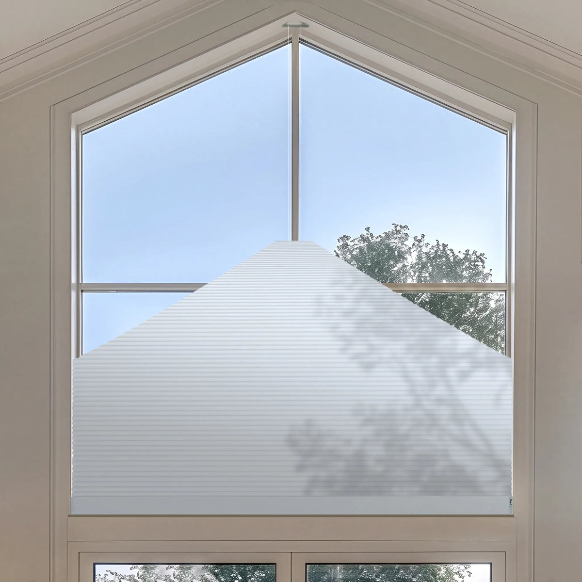 A white Elongated Triangle Cellular Shades installed on a large arched window, shown with natural light and outdoor tree shadows.