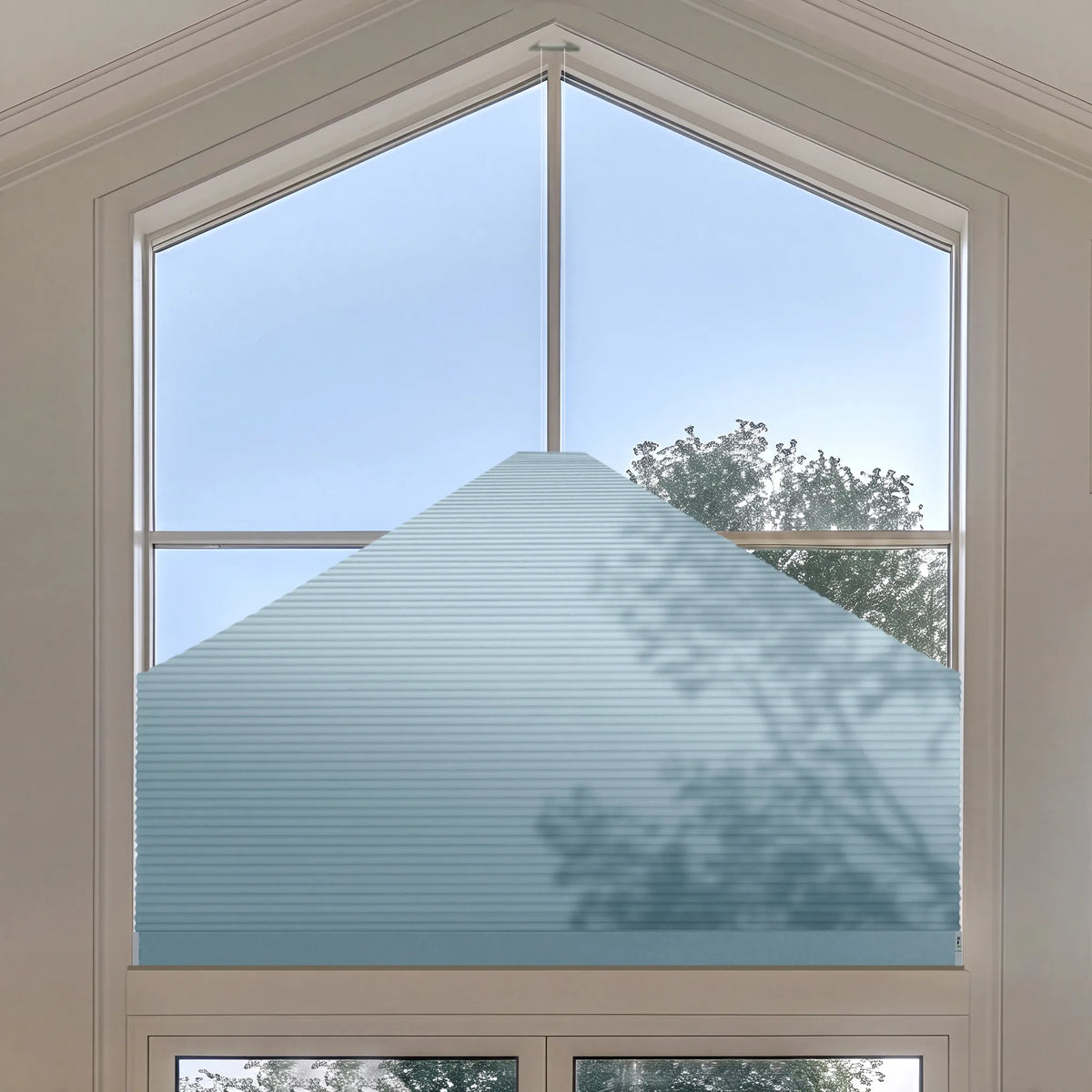 A light blue Elongated Triangle Cellular Shades installed on a large arched window, with outdoor sky and tree branches visible through the glass.