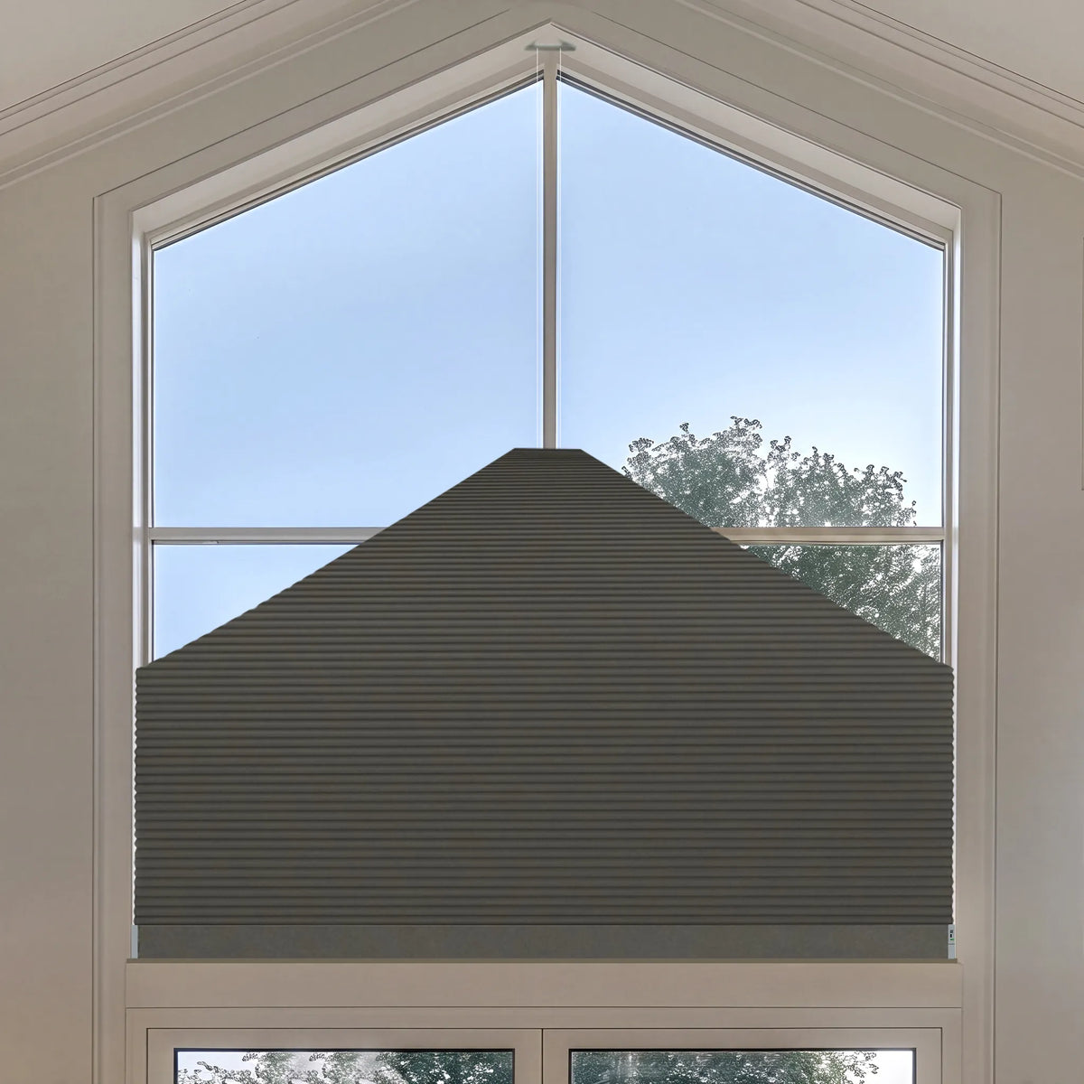 A dark gray Elongated Triangle Cellular Shades installed on a large arched window, shown from a top-down view with a light blue sky and trees visible outside.