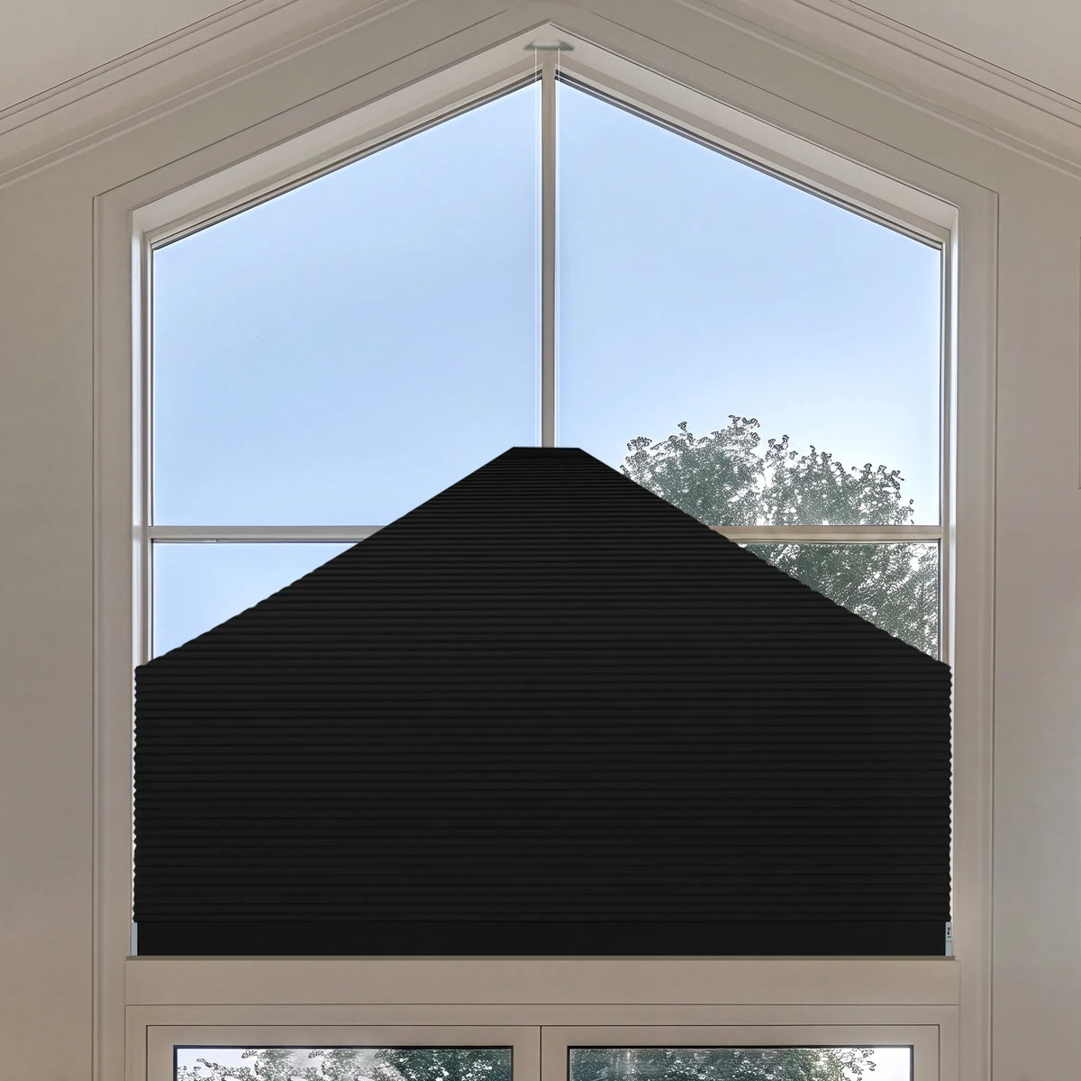 A black Elongated Triangle Cellular Shades installed on a tall arched window, shown from the inside looking out toward the sky and trees.