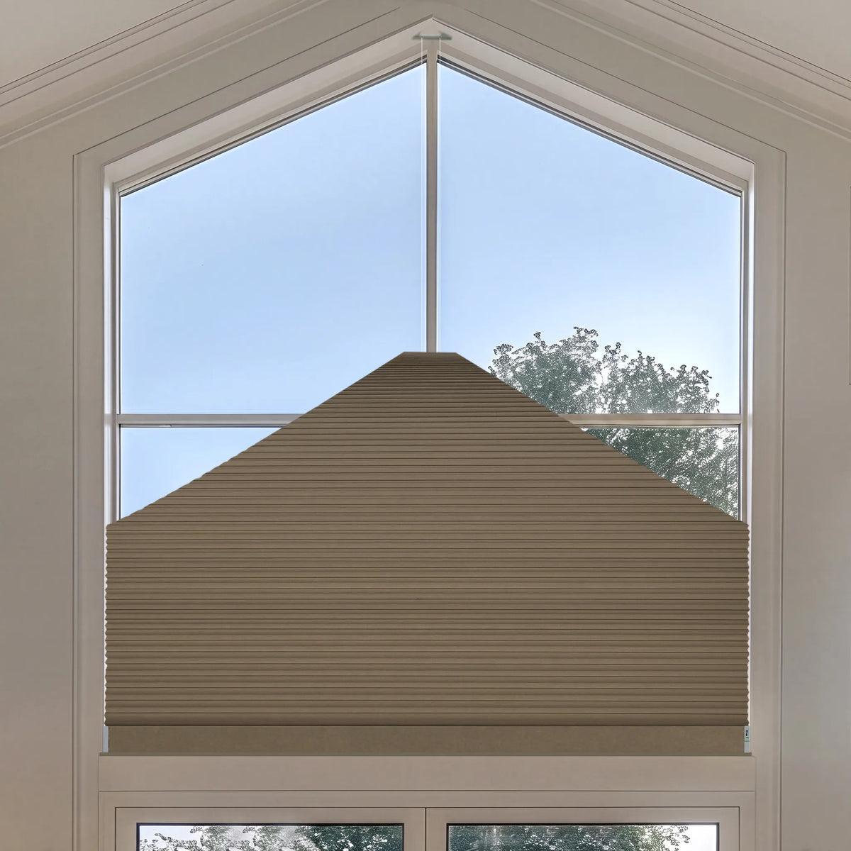 A brown Elongated Triangle Cellular Shades installed on a tall, multi-pane window, shown from a top-down angle with a view of the blue sky and trees outside.