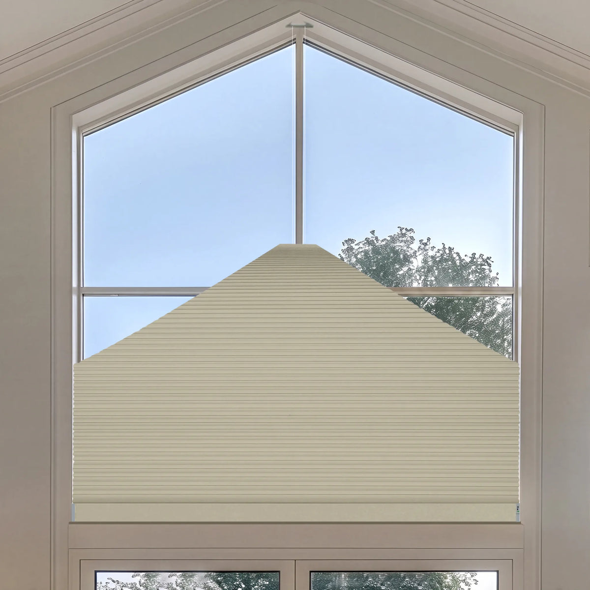 A cream-colored Elongated Triangle Cellular Shades installed on a large arched window, shown with a view of blue sky and trees outside.