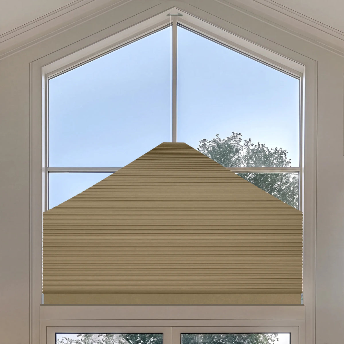 A beige Elongated Triangle Cellular Shades installed on a large arched window, shown from a top-down angle with sky and trees visible outside.