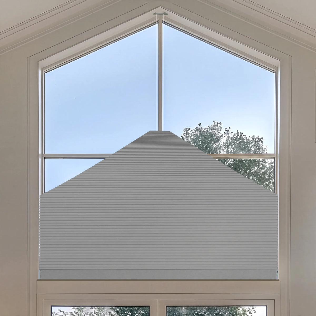 A large white Elongated Triangle Cellular Shades installed on a tall, multi-pane window with a triangular top, shown from a high angle looking out towards the sky and trees.