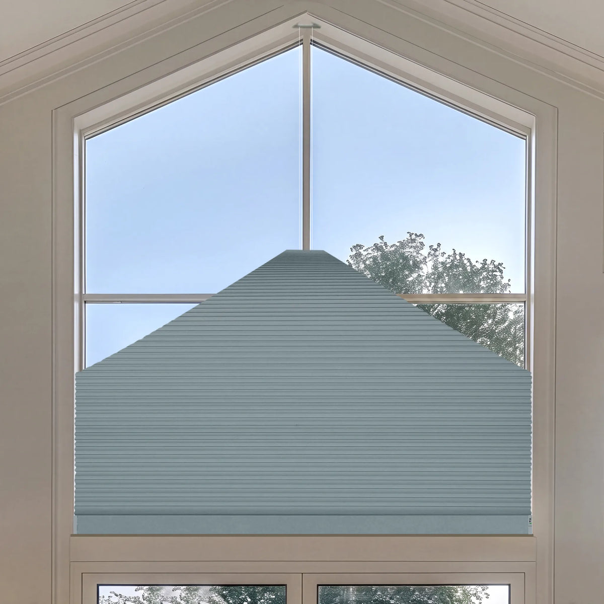 A light blue-gray Elongated Triangle Cellular Shades  installed on a large arched window, shown from a top-down view with a view of the sky and trees outside.