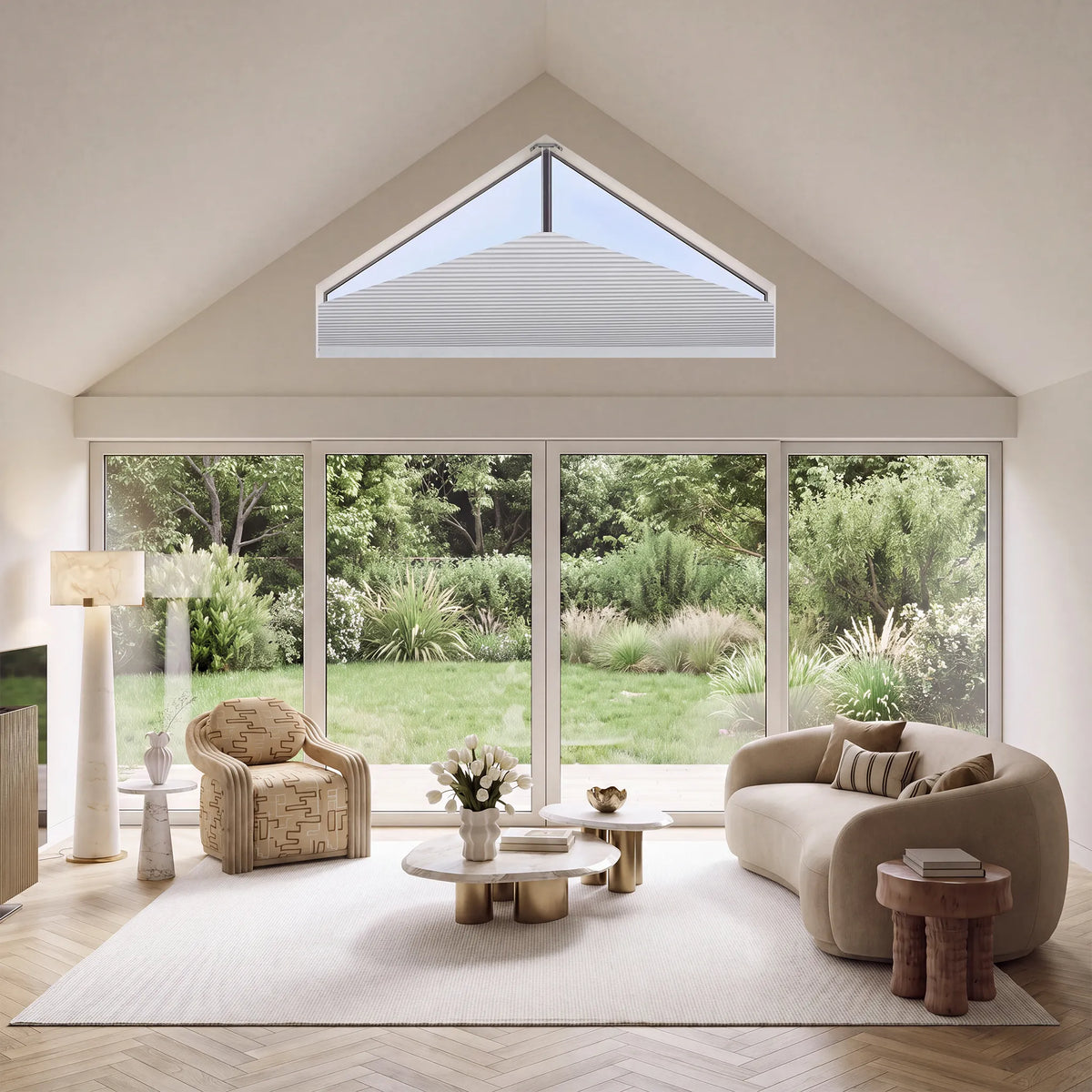 A modern living room with a curved beige sofa, patterned armchair, wooden coffee tables, and a large white sElongated Triangle Cellular Shades installed in a gabled roof, overlooking a green garden.