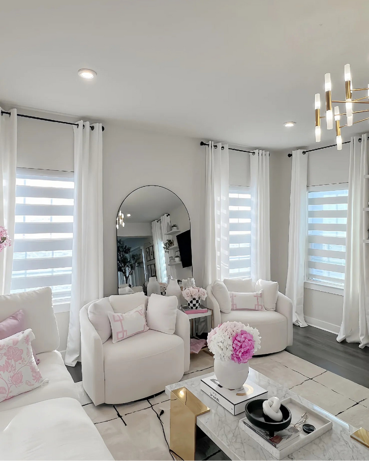 Bright white living room with multiple windows featuring zebra shades (sheer dual shades) and floor-to-ceiling white curtains.