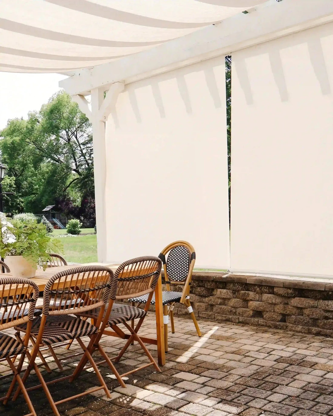 An outdoor patio area under a white pergola featuring large cream-colored smart outdoor weather shades.