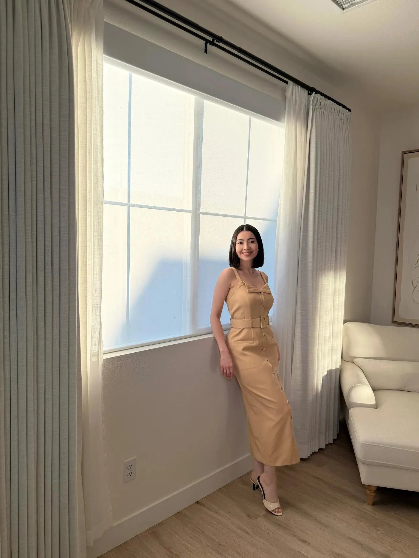 A modern interior featuring a woman standing by a large window equipped with a smart semi-sheer roller shade and white side drapes.