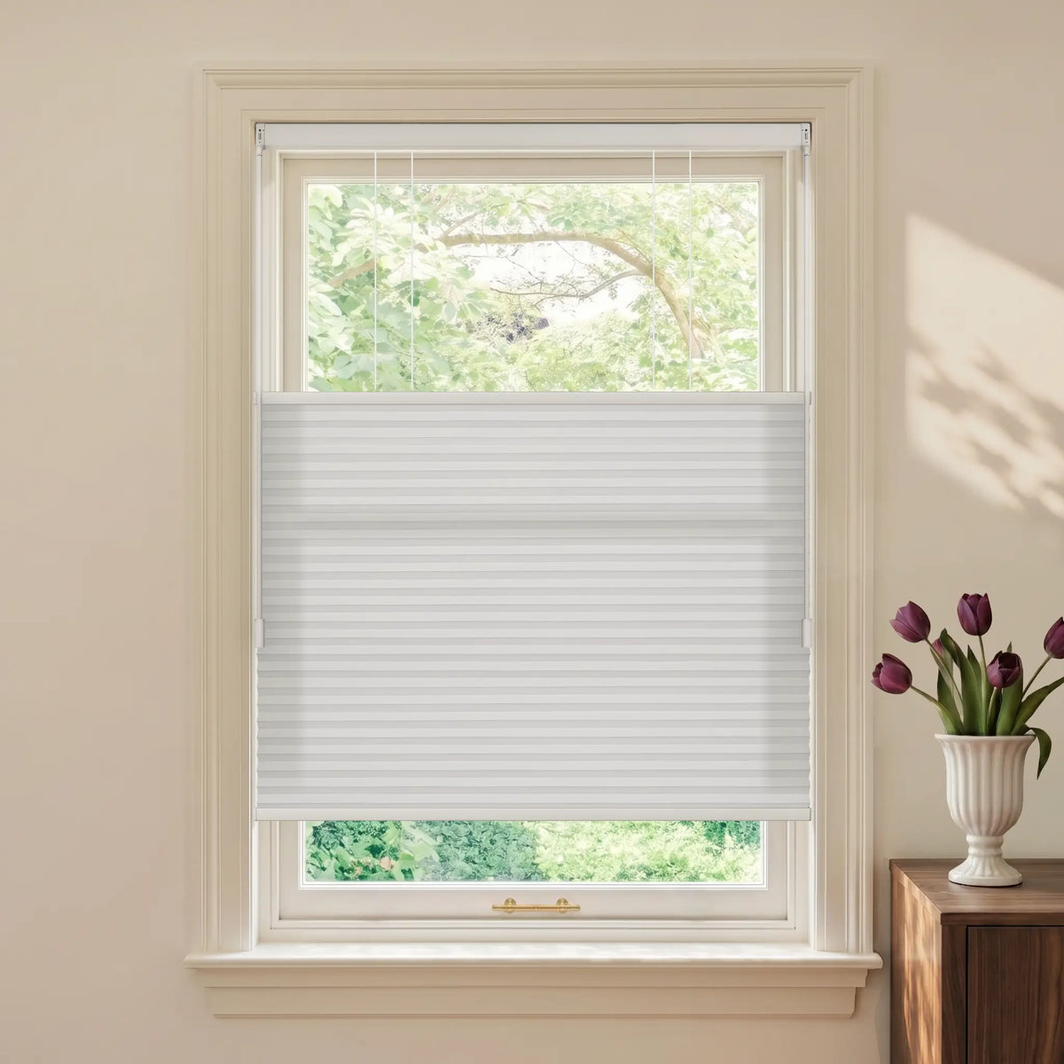 White Motionblinds Smart Top Down Bottom Up Cellular Shades  partially drawn across a white-framed window, shown in a styled room setting with a vase of purple tulips on a wooden side table.