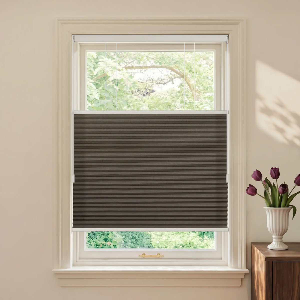A dark brown Motionblinds Smart Top Down Bottom Up Cellular Shades installed in a white window, shown in a styled room with a vase of purple tulips on a wooden side table.