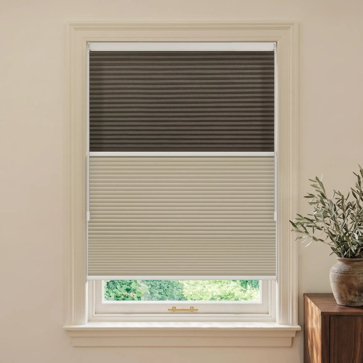 A Motionblinds smart Day Night Cellular Shades  with the top half in dark brown and the bottom half in light beige, installed on a white-framed window in a warm beige room.