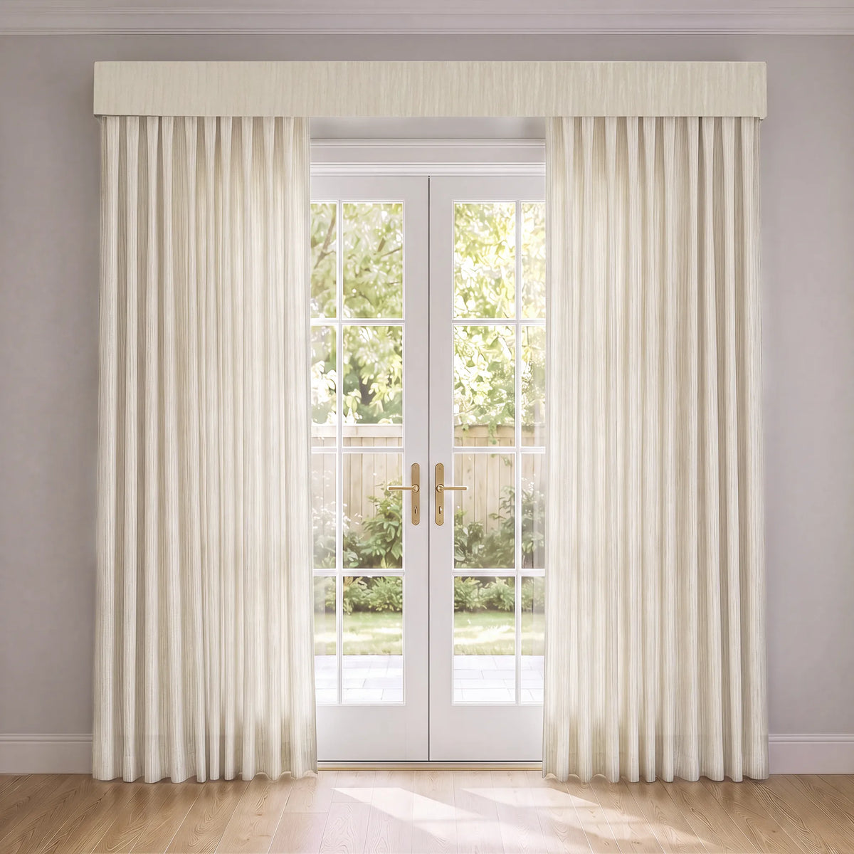 A pair of long cream-colored pleated curtains with a matching fabric valance, hung on either side of white French doors showing a garden view.