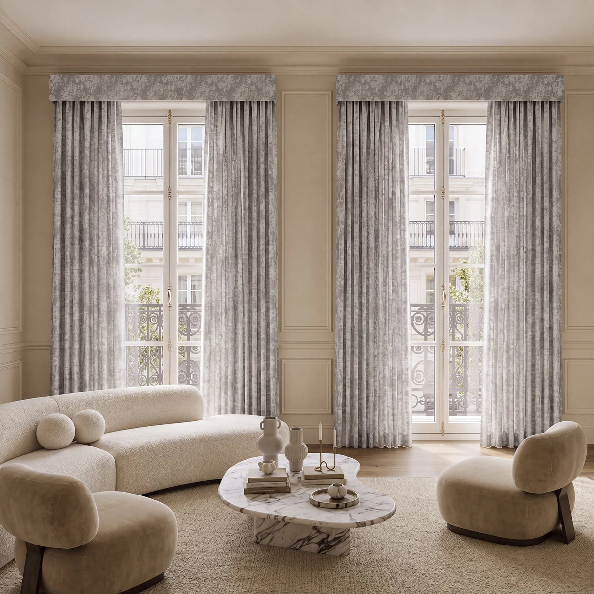 A luxury living room featuring two tall window treatments with a gray and white damask pattern, styled with a cream curved sofa, a matching accent chair, and a marble coffee table.