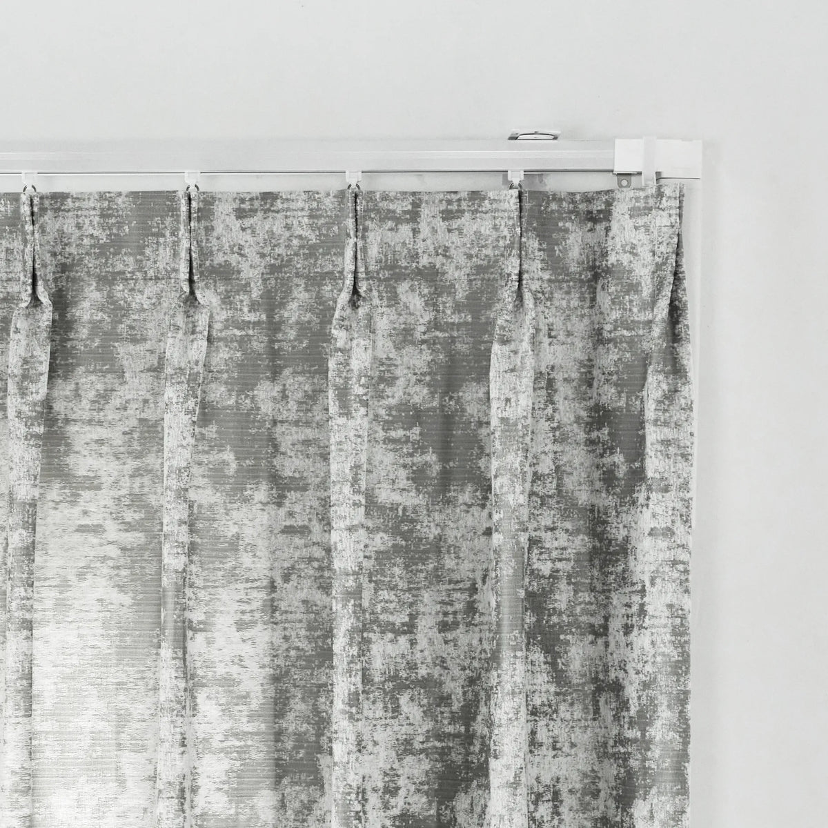 A single curtain panel hanging from a white rod against a plain white wall. The fabric has a distressed, mottled gray and white texture.