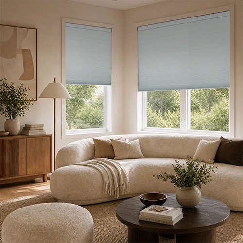 A styled living room with two white cellular shades, a cream curved sectional sofa, a wooden sideboard, and a round coffee table.