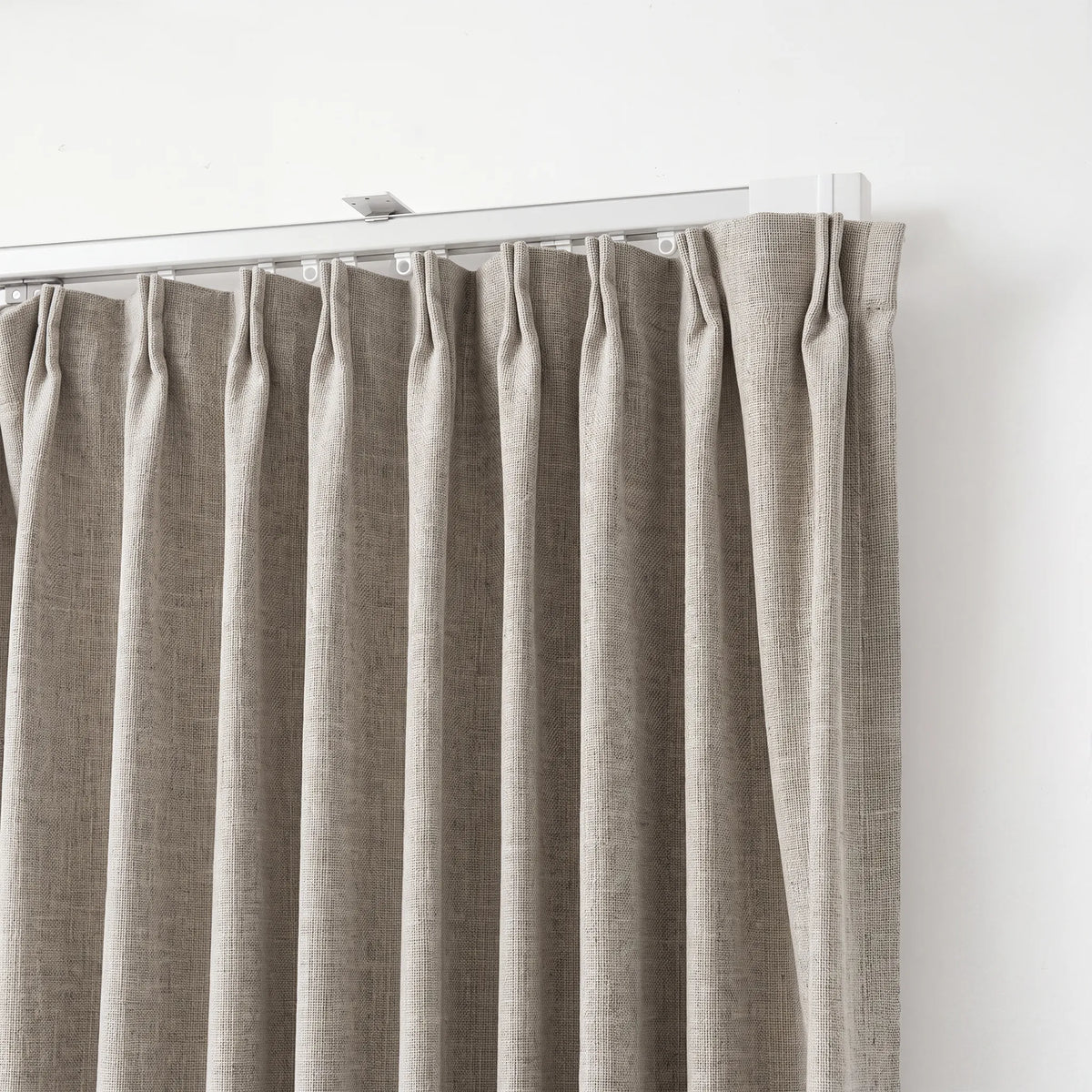 A close-up of a light beige linen curtain panel hanging from a silver metal rod against a plain white wall.