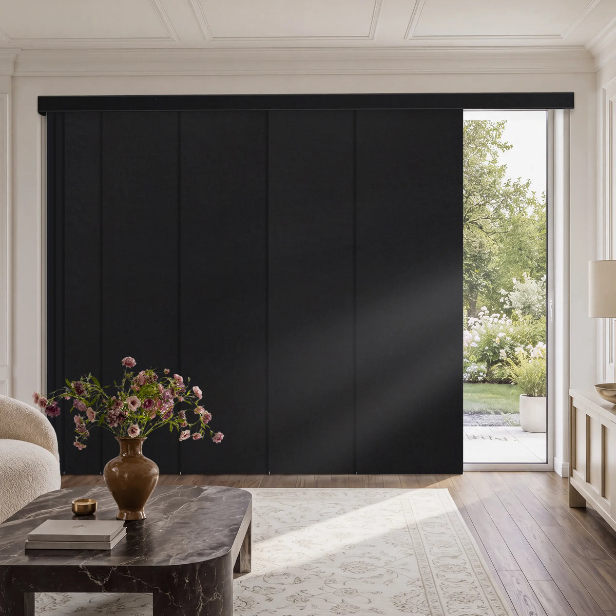 A large black Motorized Blackout Panel Track Blinds  installed in a bright, elegant living room with hardwood floors, a marble coffee table, and a view of greenery outside.