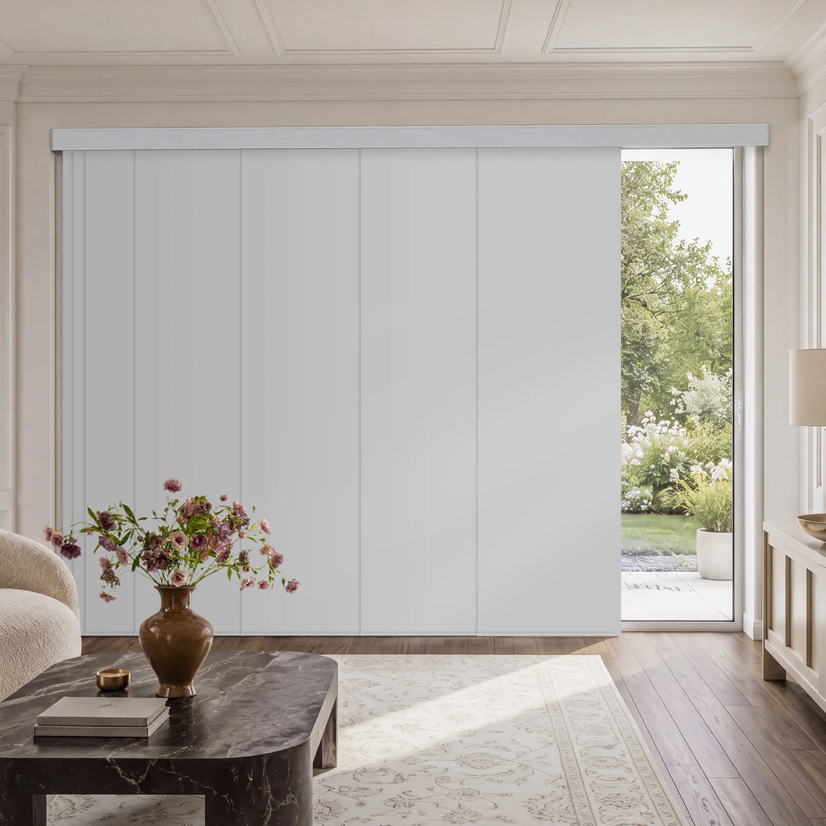A large white Motorized Blackout Panel Track Blinds set in a bright, elegant room with hardwood floors, a marble coffee table, and a view of a green garden outside.