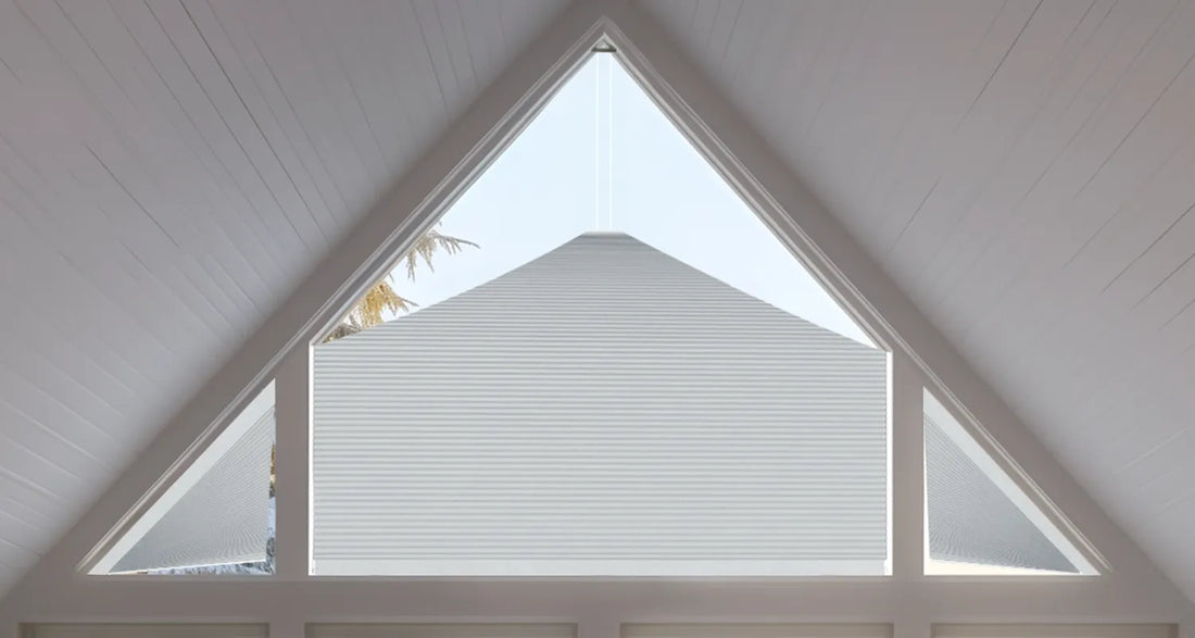 White Motorized Elongated Triangle Cellular Shades installed in a large triangular skylight on a white wood-paneled ceiling.