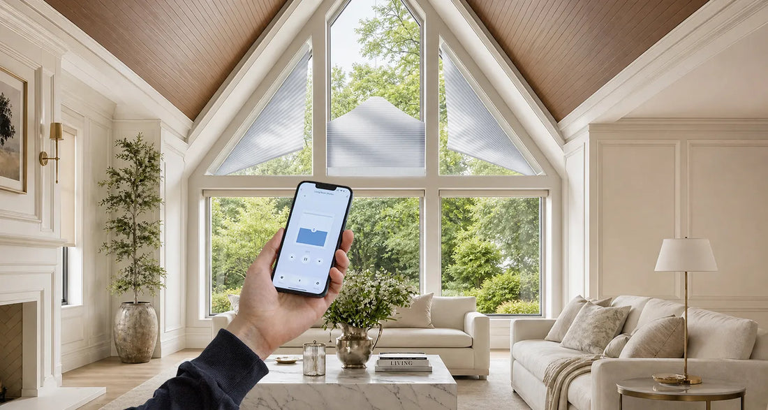 A hand holds a smartphone showing a smart home app interface in a bright, modern living room with large arched windows, cream walls, a sofa, and a wood ceiling.