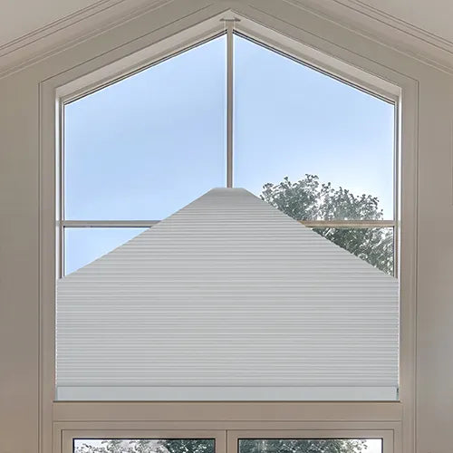 A Motorized Elongated Triangle Cellular Shades installed on a large arched window, shown from a top-down angle with a view of the blue sky and trees outside.
