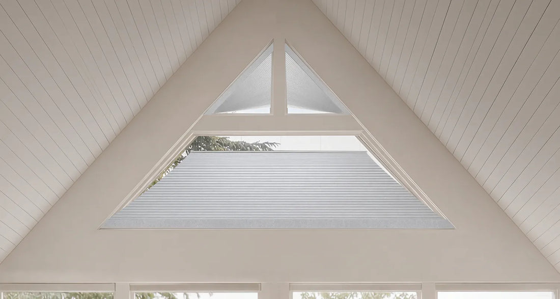A close-up view of white Motorized Isosceles Trapezoid Cellular Shades installed inside a large triangular skylight set into a white paneled ceiling.
