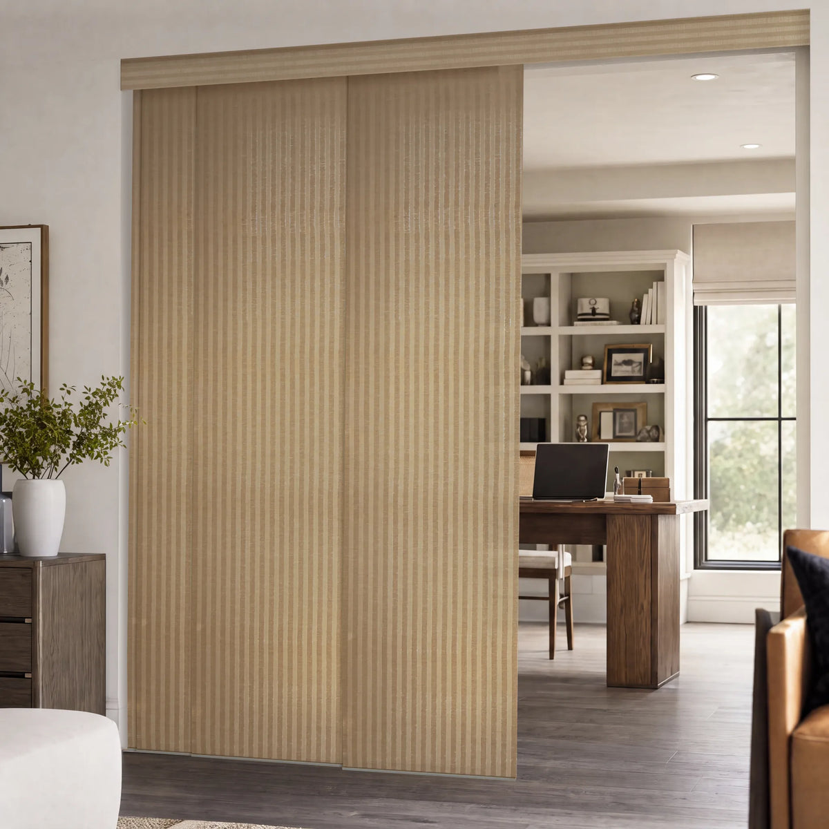 Motorized Light Filtering Panel Track Blinds in a light natural wood finish, shown installed in a modern home office setting.