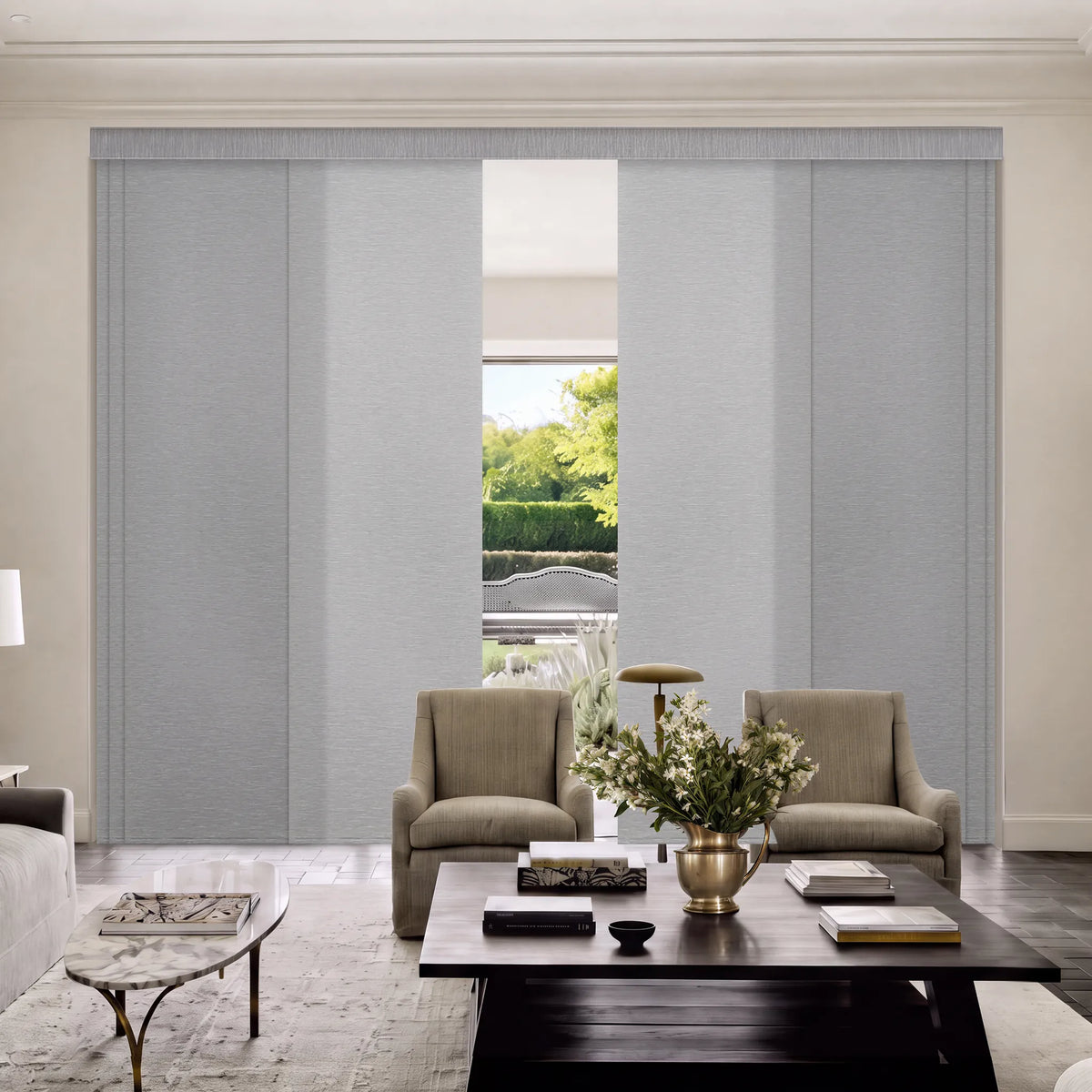 A pair of light gray fabric Motorized Light Filtering Panel Track Blinds hanging in a modern living room setting with a coffee table, armchairs, and a vase of flowers.