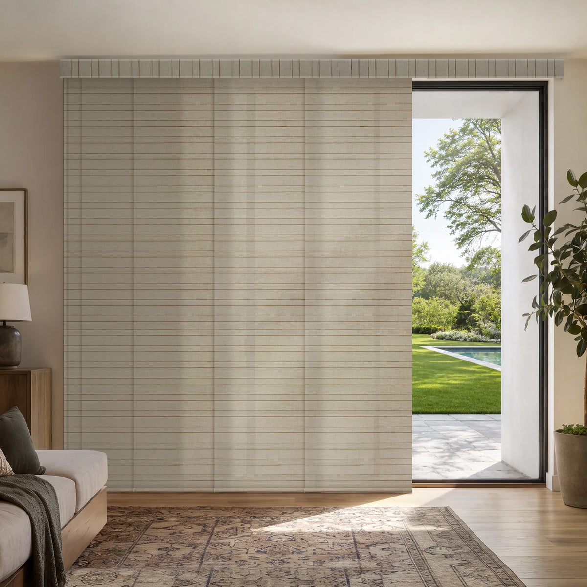 A set of Motorized Light Filtering Panel Track Blinds in a light beige tone with a subtle horizontal slatted texture, shown installed on a glass door in a modern, sunlit living room with a pool visible outside.