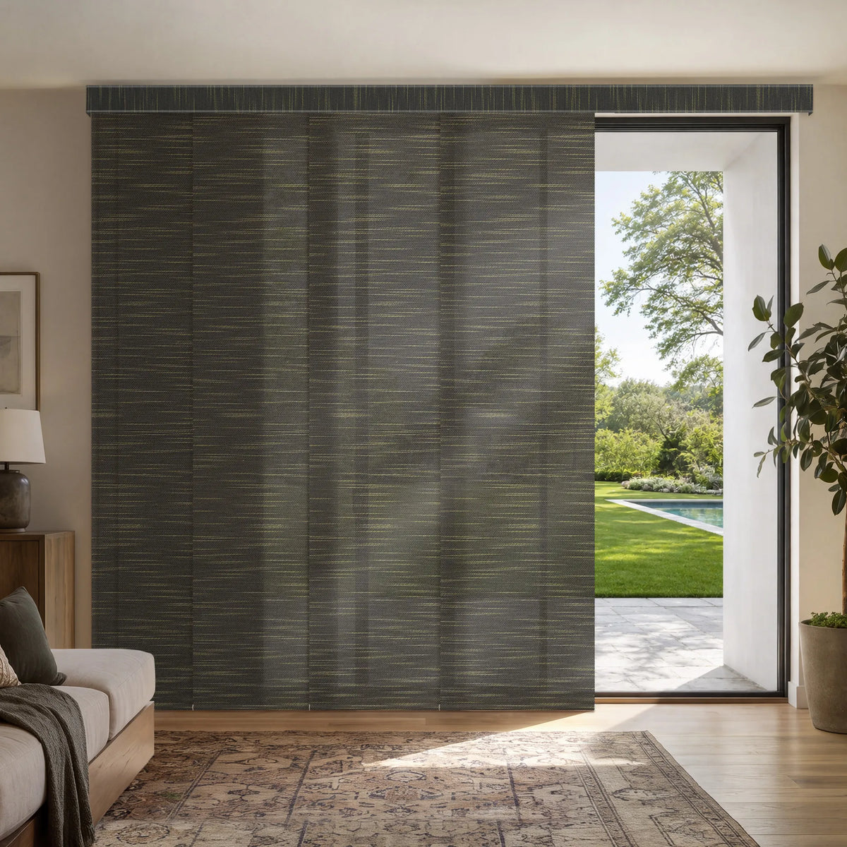 A pair of dark gray textured rMotorized Light Filtering Panel Track Blinds shown installed on a sliding door in a modern living room, with a pool garden visible outside.