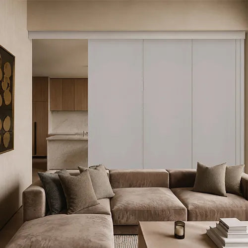 A modern living room featuring a taupe velvet sectional sofa with matching throw pillows, set against a large white sliding door and a light wood coffee table.