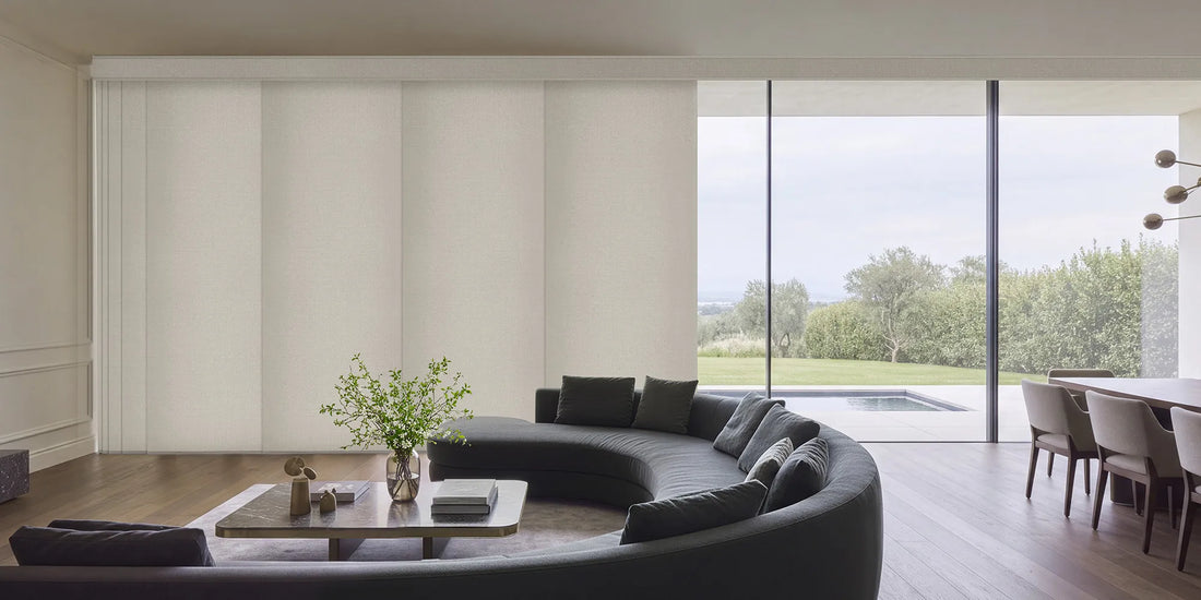 A modern curved dark gray sectional sofa in a minimalist, light-filled living room with large windows overlooking a green landscape and pool.