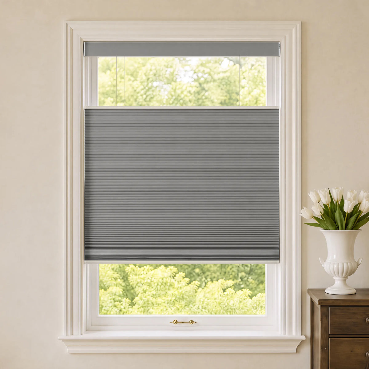 A gray Motorized Top Down Bottom Up Blackout Cellular Shades  installed in a white-framed window, shown in a styled room setting with a vase of white tulips on a wooden side table.