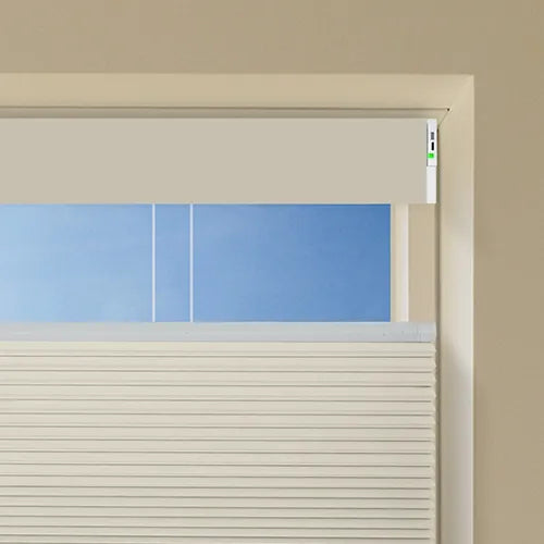 A close-up of a white Motorized Top Down Bottom Up Cellular Shades partially drawn over a window, with horizontal slats visible and a beige wall surrounding the frame.