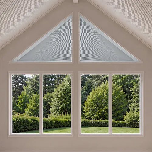 A set of white roller blind shades installed in a large, multi-pane window with a triangular gable design, showing a green garden view outside.