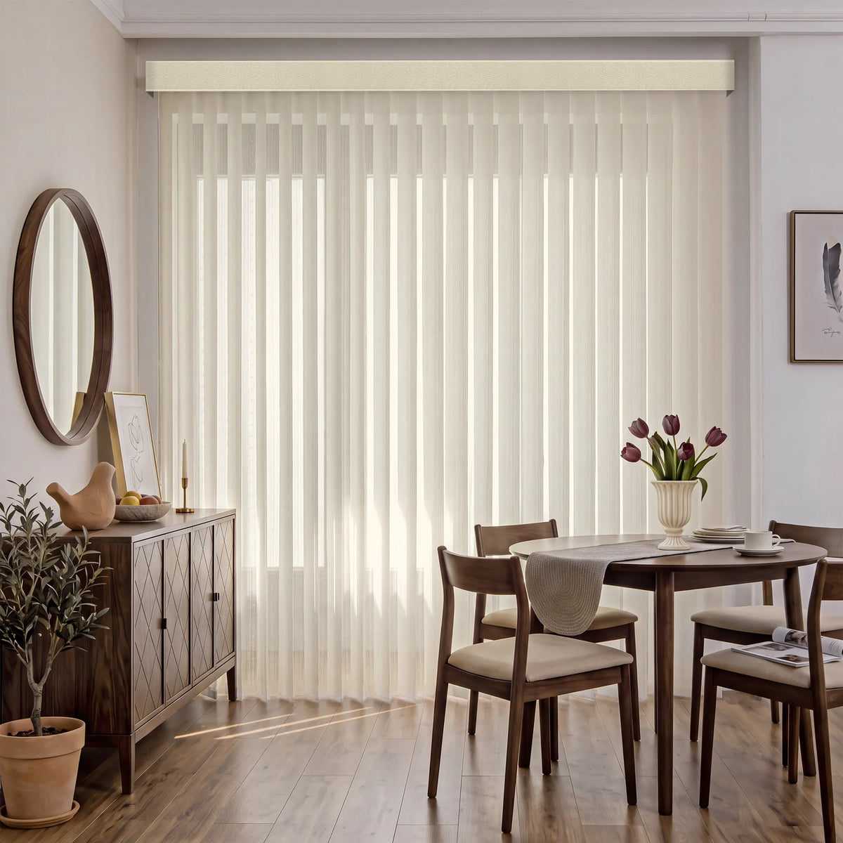 A dining room interior with tall cream Smart Sheer Vertical Blinds covering a large window, styled with a wooden dining table and chairs, a sideboard, a mirror, and a vase of tulips.