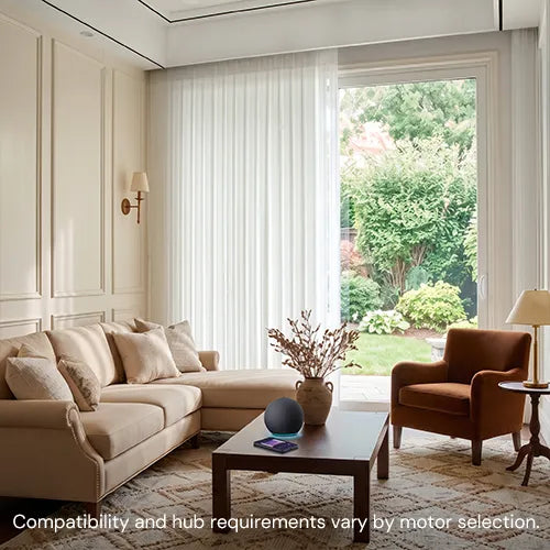 A beige sectional sofa in a bright, modern living room with cream walls, a brown accent chair, a wooden coffee table, and a large window looking out to a green garden. Text at the bottom reads: 'Compatibility and hub requirements vary by motor selection.