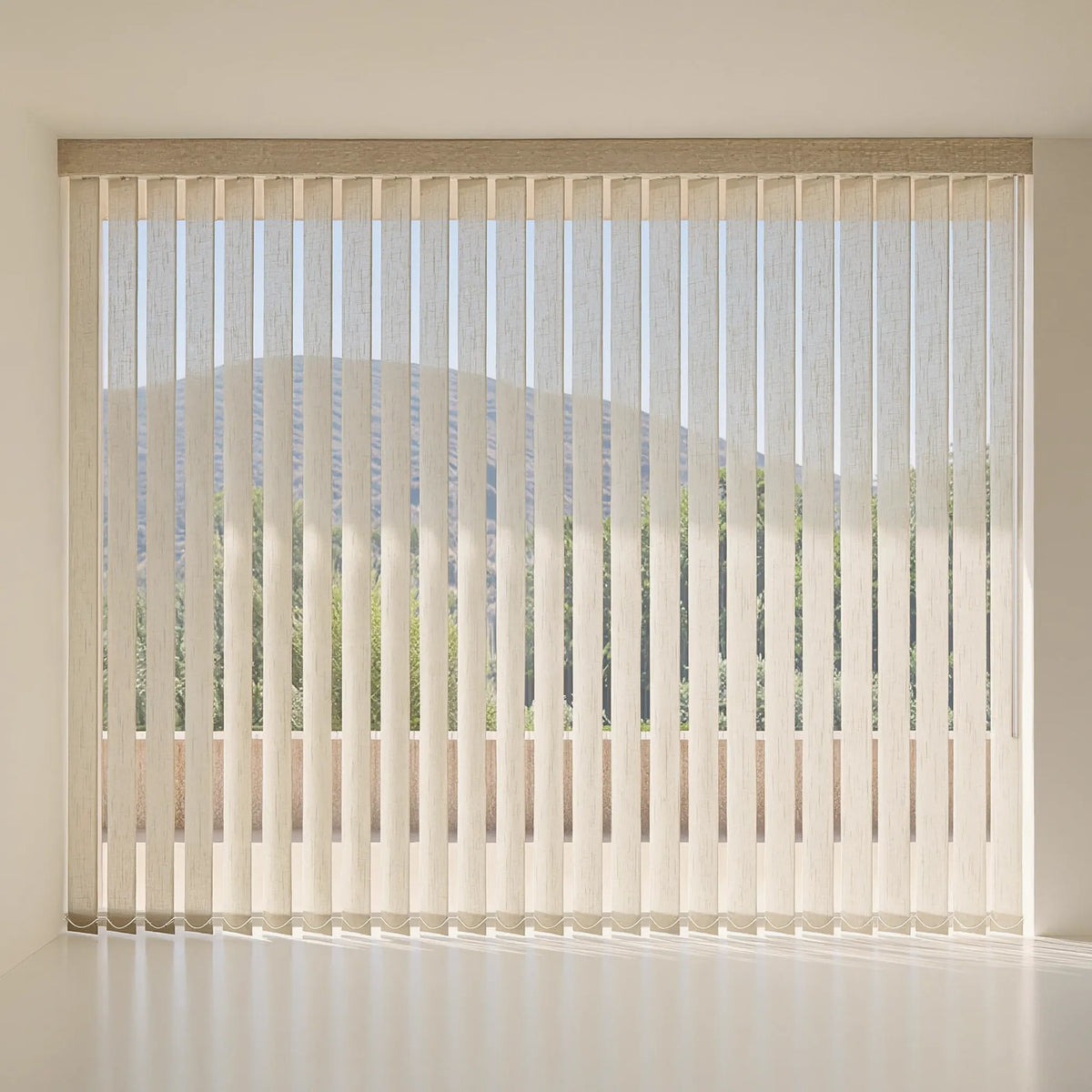 Vertical blinds in a light beige or off-white shade, hanging over a large window in a minimalist room with a soft-focus view of trees and hills outside.